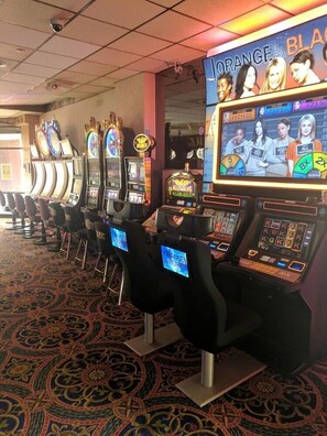 A row of slot machines with a screen displaying a game interface, and a sign above them that reads 'ORANGE IS the NEW BLACK'. - Historic Hotel Nevada and Gambling Hall (Ely)