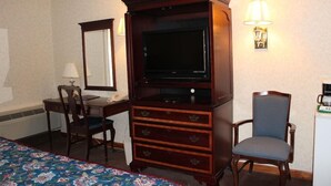 Ein Hotelzimmer mit einem Bett, einem Schreibtisch mit Stuhl, einem Fernseher auf einer Holzkommode, einer Lampe und einem kleinen Kühlschrank.