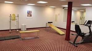 Ein Fitnessraum mit Trainingsgeräten, einer roten Säule und einem Spiegel an der Wand.