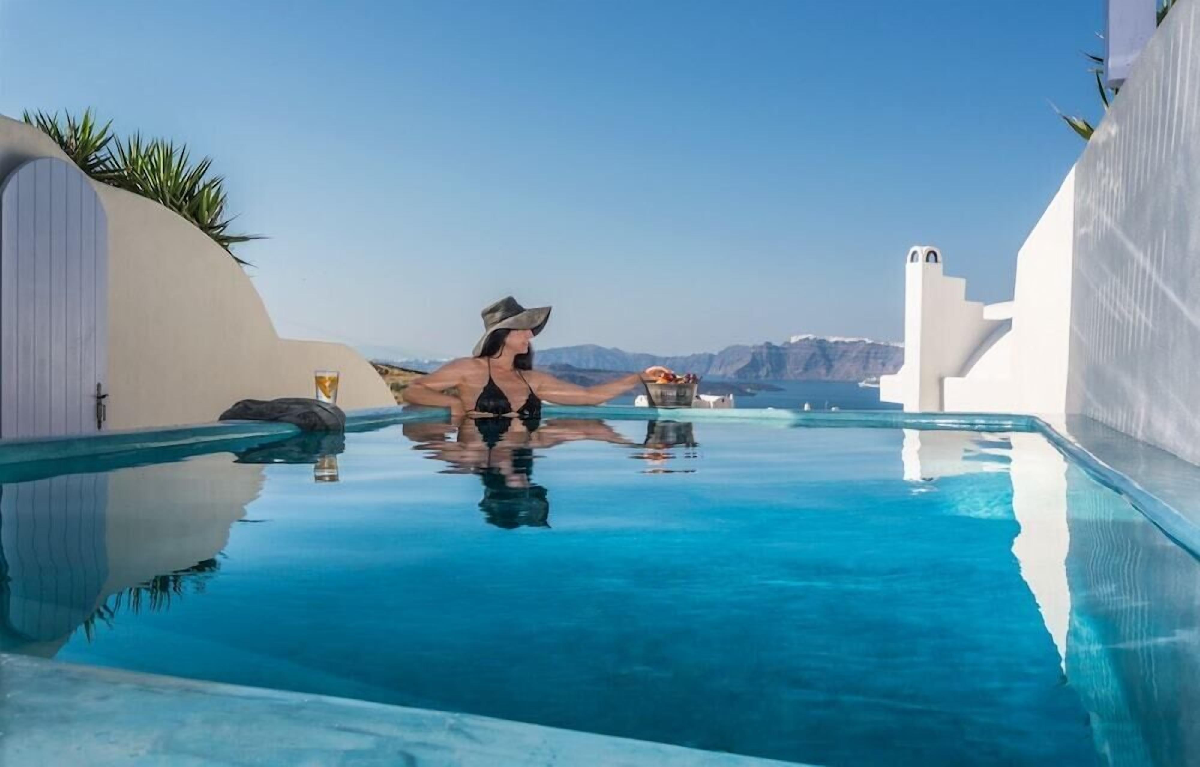 Une personne se détend dans une piscine à débordement aux eaux bleues et cristallines, avec une vue sur des montagnes lointaines.