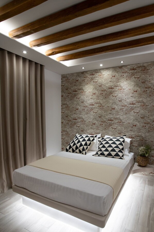 Un dormitorio moderno con una cama, vigas de madera, una pared de ladrillo y una cortina.