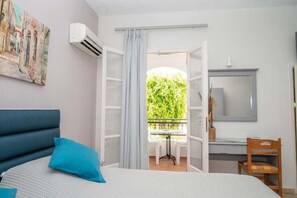 Un dormitorio con cama, escritorio y silla. Se ve vegetación por la ventana.