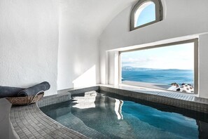 Zona de spa con vistas despejadas al mar gracias a un amplio ventanal, una pequeña piscina y un cesto de toallas.