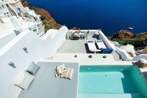 A rooftop terrace with a pool, lounge chairs, and a table with a view of the sea. - Diamond Luxury Suites (Santorini)