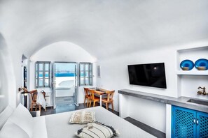 A modern hotel room with a bed, a desk, a TV, and a view of the sea. - Diamond Luxury Suites (Santorini)
