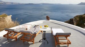 Une terrasse dotée de chaises longues en bois et d’une table, offrant une vue panoramique sur l’océan.