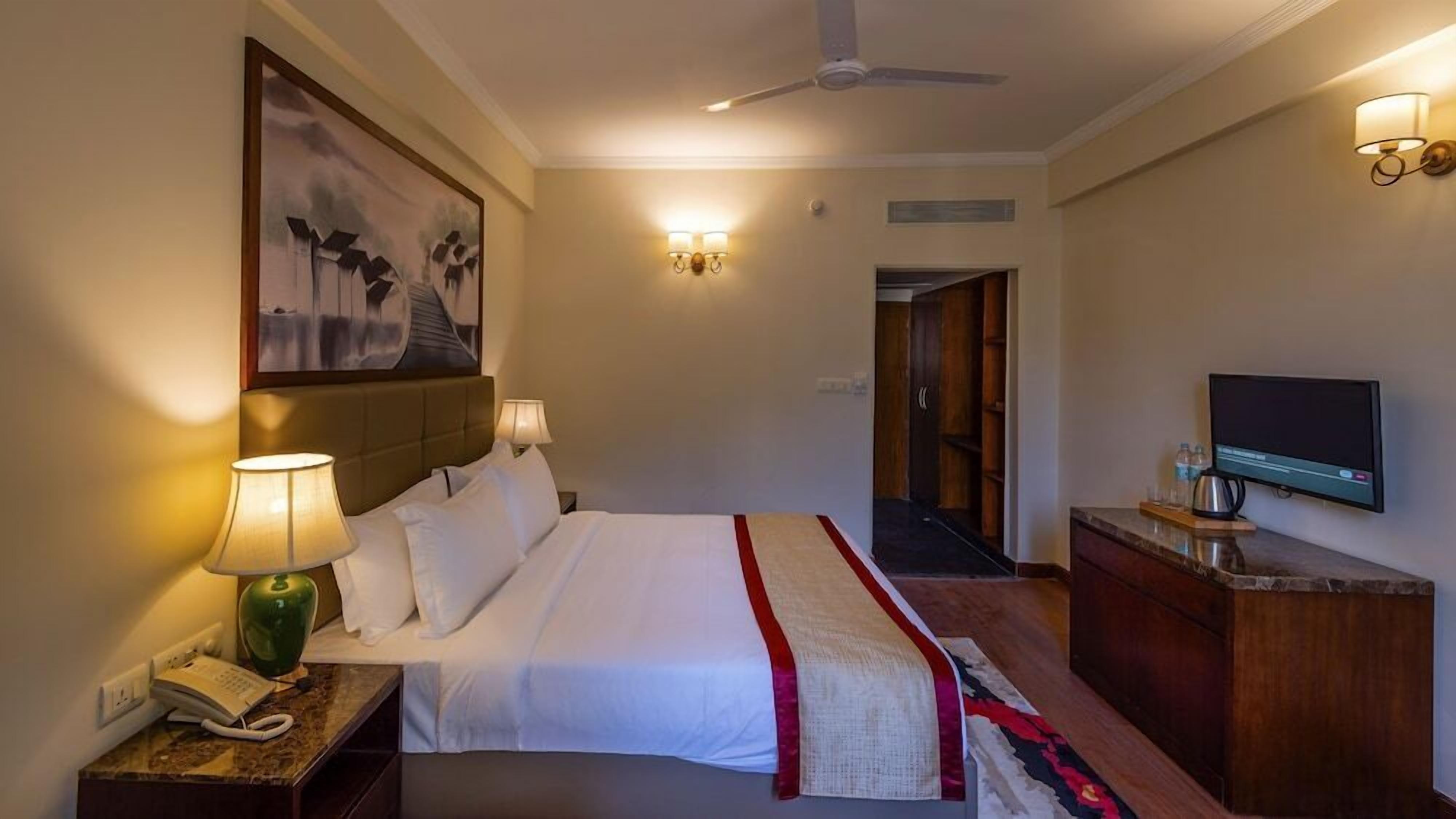 Een hotelkamer met een bed, bedlampen, een schilderij, een televisie en een bureau met telefoon.