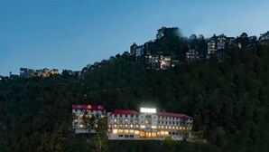 A multi-story hotel with a red roof, surrounded by dense forest, and multiple buildings on a hillside. - 8fold By Larisa Shimla (Shimla)