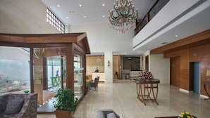 A spacious lobby with a high ceiling, a chandelier, a reception desk, and a dining area with a table and chairs. - 8fold By Larisa Shimla (Shimla)