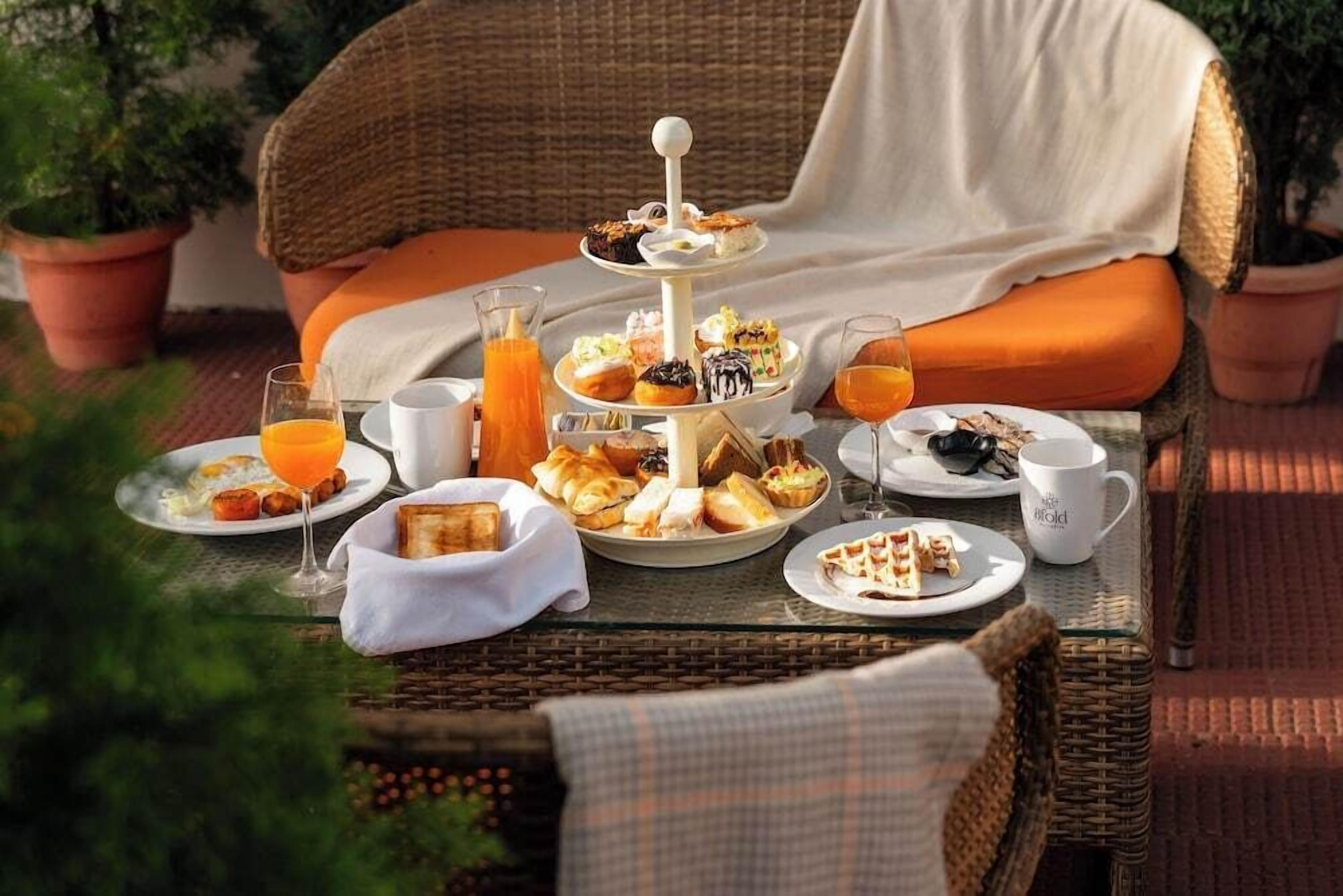 A wicker table with a tiered dessert stand, plates of food, and glasses of orange juice.