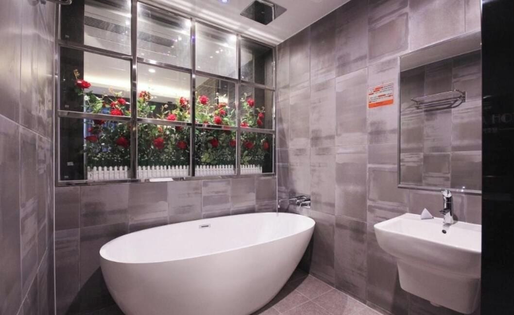 A modern bathroom with a freestanding bathtub, a sink, and a window with a view of a garden.