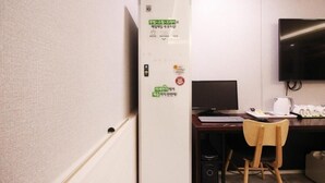 A hotel room with a desk, chair, TV, and a white refrigerator with stickers. - Le Idea Hotel (Pohang)