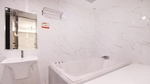 A bathroom with a marble wall, a sink, a bathtub, and a mirror. - Le Idea Hotel (Pohang)