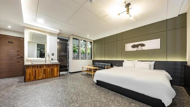 A modern hotel room with a large bed, a wooden vanity, a mirror, and a wall-mounted artwork. - Le Idea Hotel (Pohang)