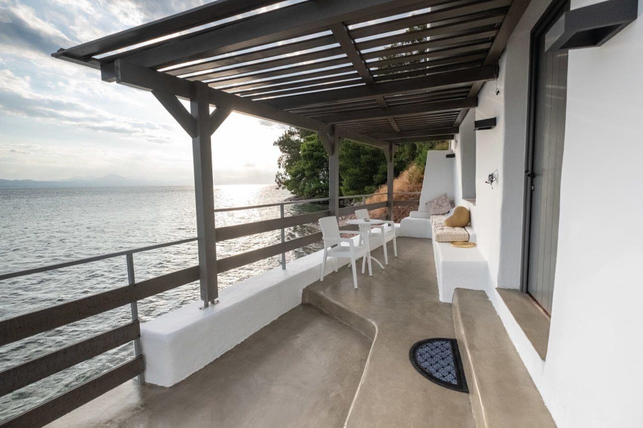 A covered outdoor seating area with white chairs and a table, overlooking a body of water.