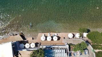 An aerial view of a beachfront property with a pool area, outdoor seating, and a wooden deck overlooking the sea.