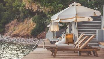 A wooden deck with lounge chairs and a wooden cabinet, overlooking a body of water.