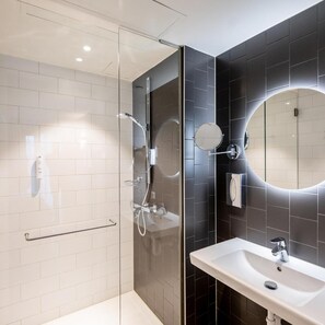 Un baño moderno con ducha envuelta en vidrio, un lavabo blanco y un espejo grande.