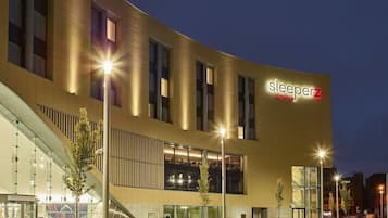 A modern hotel with a curved facade, large windows, and outdoor seating areas with planters.