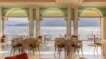 Ein Restaurant mit Tischen und Stühlen, das großzügig gestaltet ist und große Fenster mit Blick auf ein Gewässer hat.