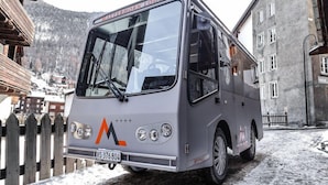 Een bus geparkeerd in een besneeuwd dorp met houten gebouwen en een berg op de achtergrond.