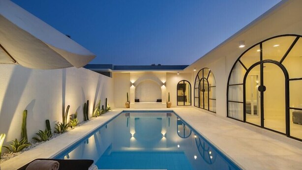 A modern indoor swimming pool with a lounge area, arched windows, and a well-lit ambiance. - The Grand Daha A Luxury Resort and Spa (Seminyak)