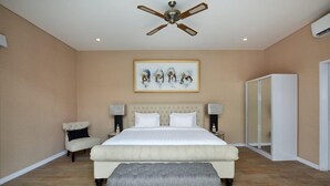 A bedroom with a large bed, a ceiling fan, a framed artwork, bedside lamps, a chair, and a wardrobe. - The Grand Daha A Luxury Resort and Spa (Seminyak)