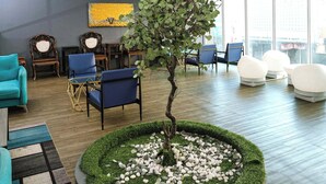 A modern lounge with a central tree, round seating, and a large window. - Palette Georgetown Formerly WoW Hotel (George Town)