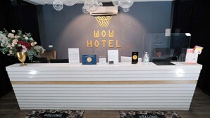 A hotel reception desk with a 'WOW HOTEL' sign, a welcome mat, and a reception counter with various informational brochures and a small plant. - Palette Georgetown Formerly WoW Hotel (George Town)