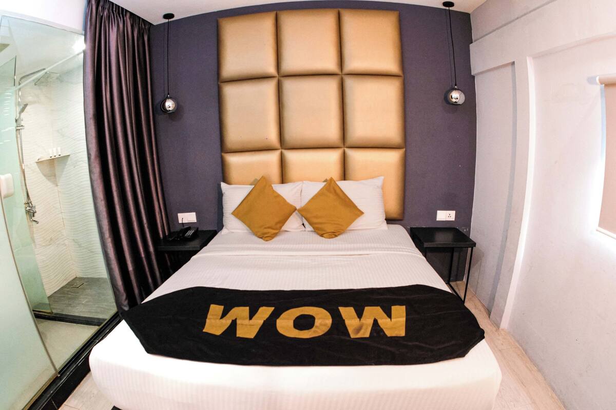 A hotel room with a large bed, a headboard with a padded design, two bedside tables, and a glass shower enclosure.