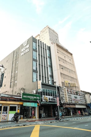 A multi-story building with a prominent 'WOW HOTEL' sign, a storefront with a green awning, and a street with pedestrians. - Palette Georgetown Formerly WoW Hotel (George Town)