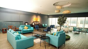A modern lounge with teal sofas, a coffee table, and a large window offering a city view. - Palette Georgetown Formerly WoW Hotel (George Town)