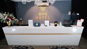A hotel reception desk with a 'WOW HOTEL' sign, a welcome mat, and a reception counter with various informational brochures and a small plant. - Palette Georgetown Formerly WoW Hotel (George Town)