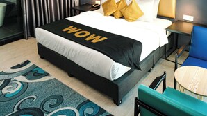 A modern hotel room with a large bed, a headboard, a bedside table, a chair, a small table, and a large window with curtains. - Palette Georgetown Formerly WoW Hotel (George Town)