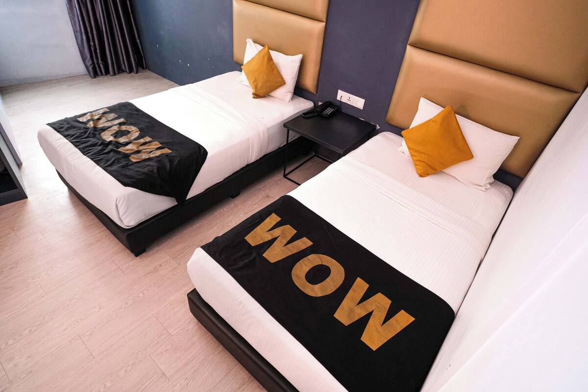 Two twin beds with black and white bedding and 'WOW' text, a bedside phone, and a wall-mounted outlet.
