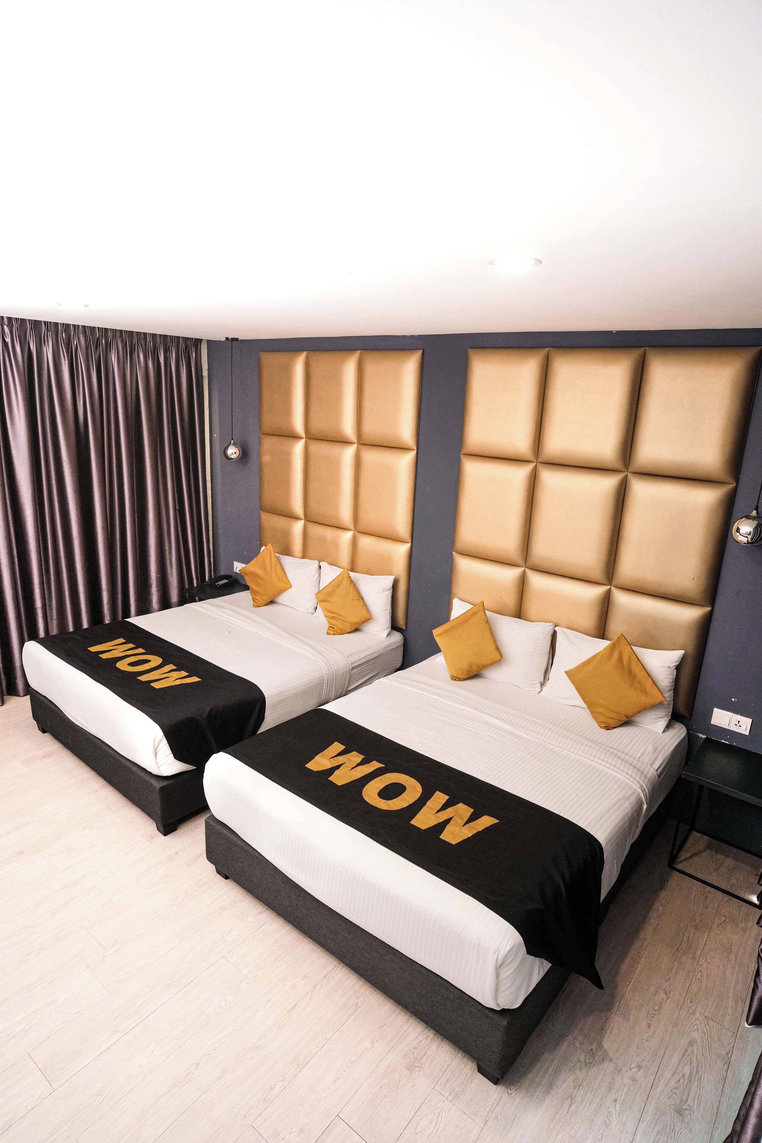 A hotel room with two beds, each with a headboard and a 'WOW' sign on the bedspread.