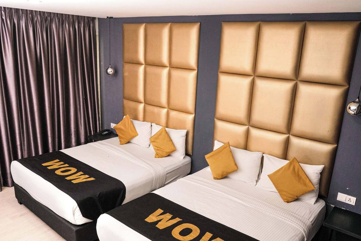 A hotel room with two beds, each with a headboard and a 'WOW' sign on the bedspread.