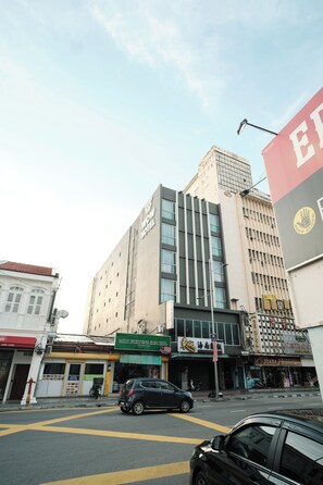 A multi-story building with a prominent 'WOW HOTEL' sign, a storefront with 'MUJI' branding, and a street with parked cars. - Palette Georgetown Formerly WoW Hotel (George Town)