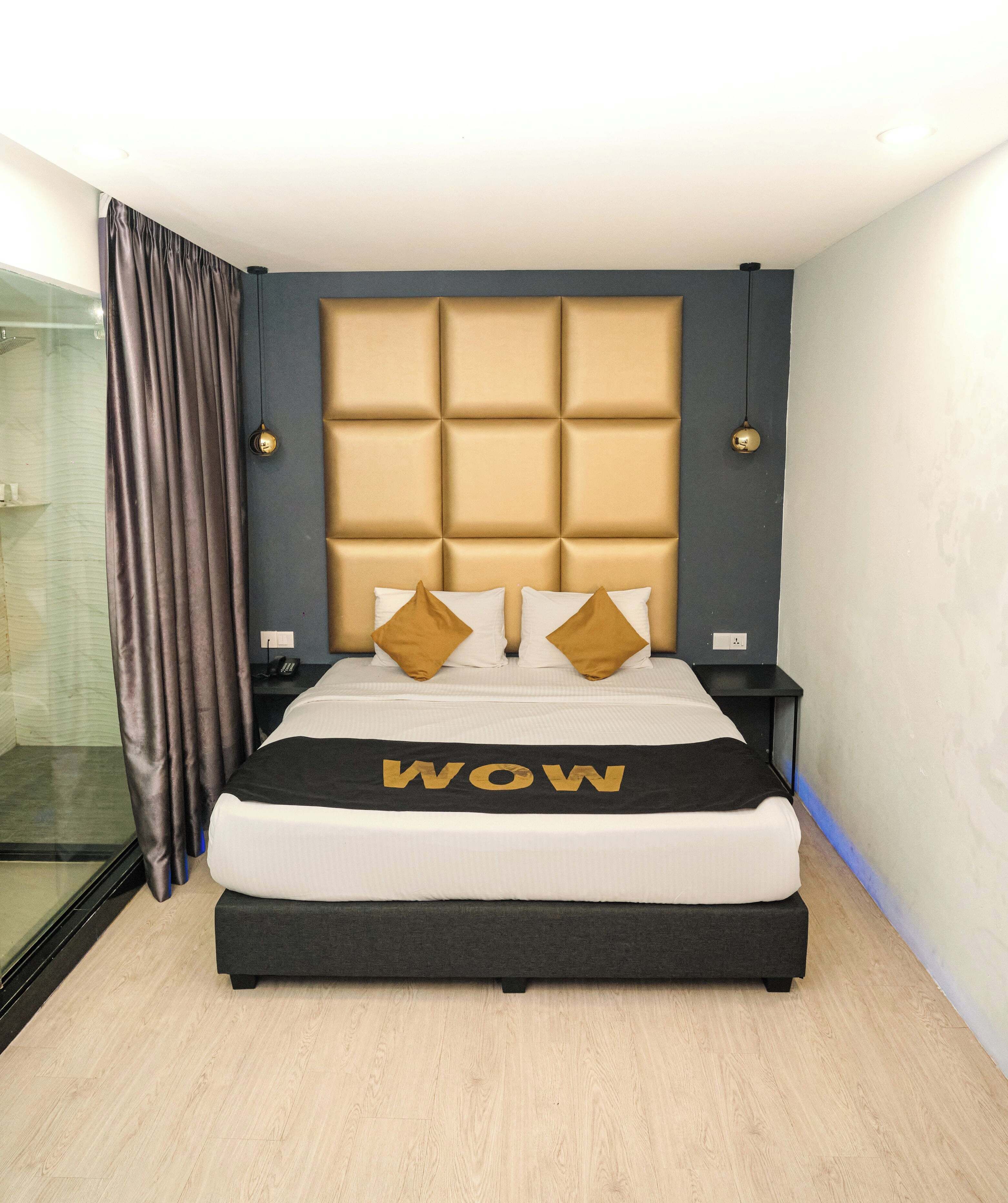 A modern hotel room with a large bed, a headboard with a padded design, two bedside lamps, and a bedside table.