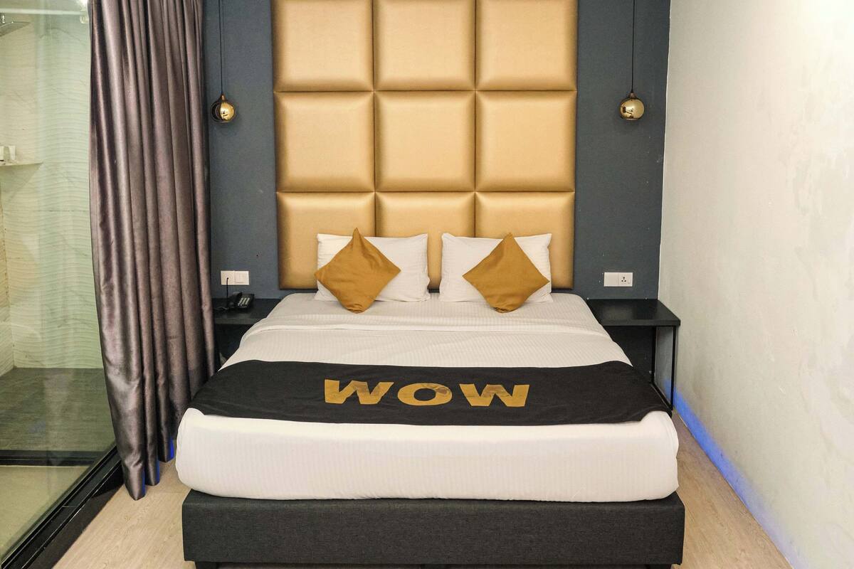A modern hotel room with a large bed, a padded headboard, two bedside lamps, and a bedside table.