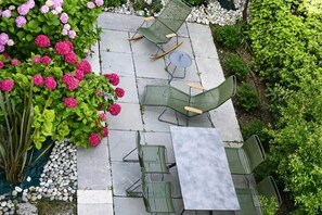 Eine Terrasse mit grünen Stühlen und einem Tisch, umgeben von Pflanzen und Blumen.