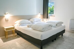 Ein ordentlich bezogenes Bett mit weißen Leinen, ein Nachttisch und ein Beistelltisch.