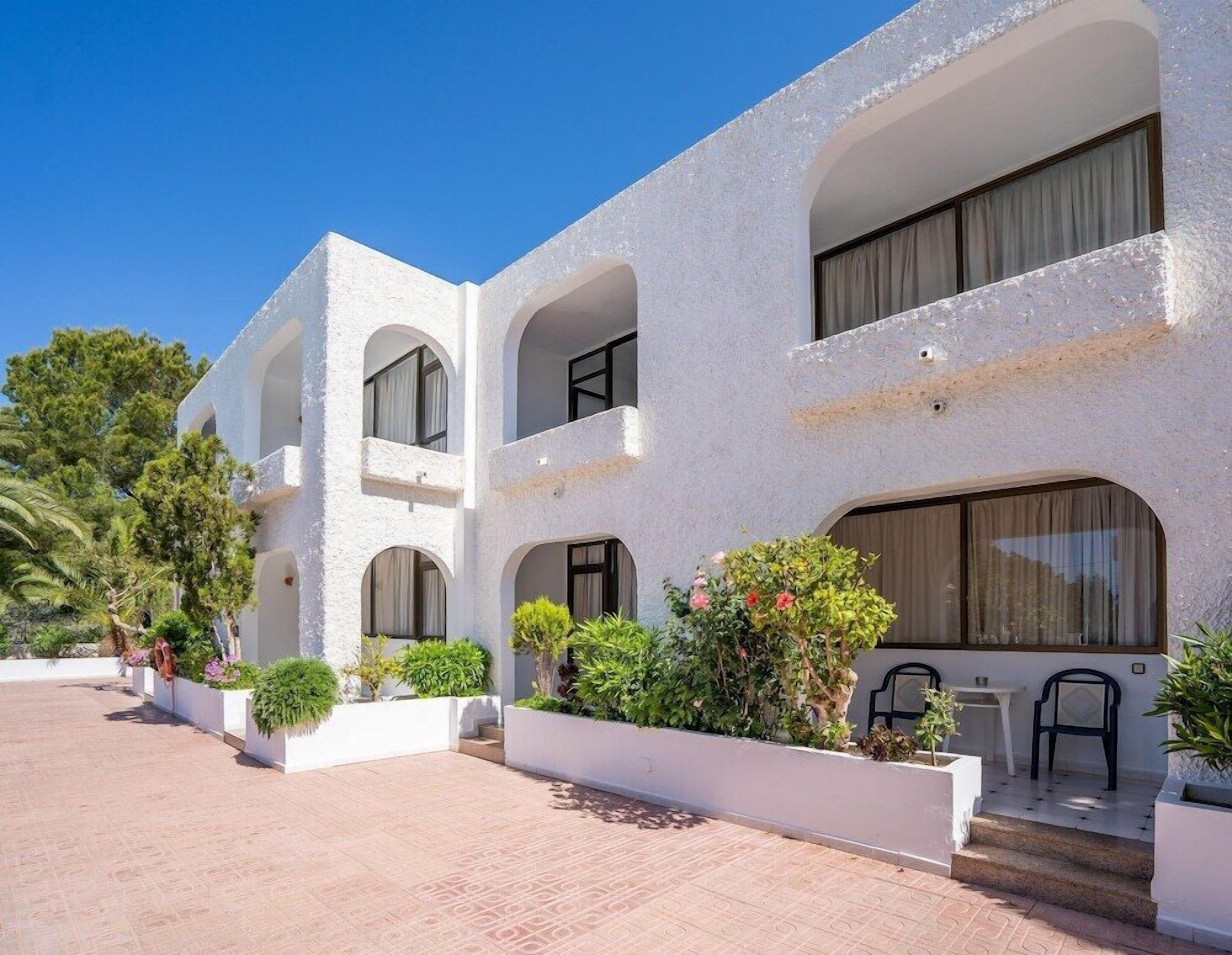 Un edificio moderno con varios balcones, paredes exteriores blancas y un patio empedrado.