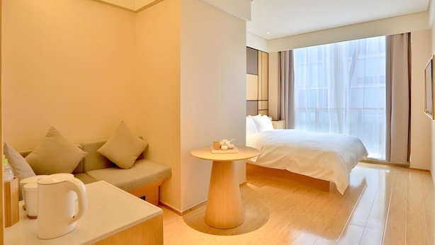 A hotel room with a bed, a sofa, a small table with a tray of items, and a window with curtains. - JI Hotel Hangzhou Qianjiang Xincheng (Hangzhou)