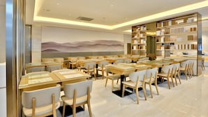A modern restaurant interior with wooden tables and chairs, a large mural on the wall, and a bookshelf with books and decorative items. - JI Hotel Hangzhou Qianjiang Xincheng (Hangzhou)