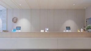 A hotel reception desk with a modern design, featuring a logo on the wall and two digital kiosks for guest services. - JI Hotel Hangzhou Qianjiang Xincheng (Hangzhou)