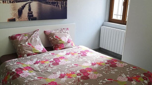 A bedroom with a bed, floral bedding, a cityscape painting, and a window with a view. - Le Cocon des Monts dOr (Saint-Germain-au-Mont-d'Or)