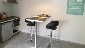 A modern kitchen with a dining area, including a table with two bar stools, a pendant light, and a wall-mounted sign with French phrases. - Le Cocon des Monts dOr (Saint-Germain-au-Mont-d'Or)