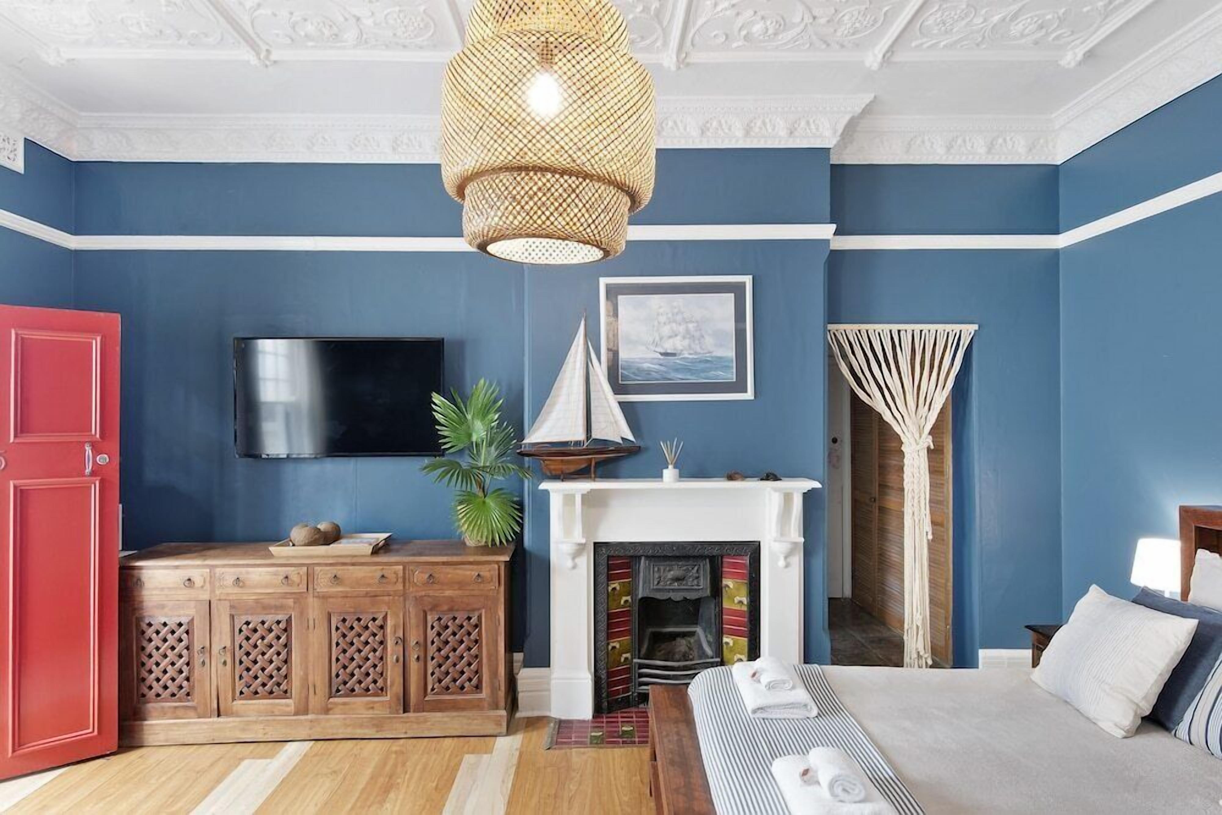 A room with a blue wall, a wooden cabinet, a fireplace, a bed, and a television.