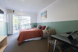 Habitación de hotel con cama, escritorio con computadora portátil, silla y ventana con vista a zonas verdes.